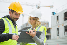 Builders In Hardhat With Tablet At Construction