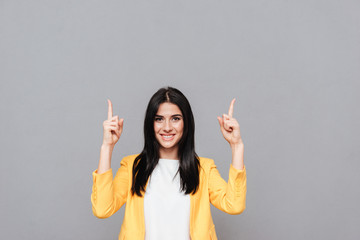 Cheerful happy woman pointing up over grey background