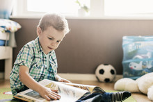 Boy Reading Book While Sitting On Floor At Home
