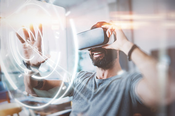 Concept of digital screen,connection and interfaces.Beraded hipster enjoyingvirtual reality glasses in modern design home studio.Smartphone use with VR goggles headset.Horizontal,flare,blurred.