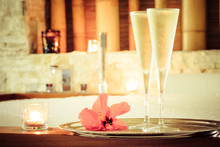 Two glasses of champagne with candle and red flower near jacuzzi