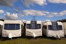 Three Caravans Stored In Rows On A Sunny Day With Clouds In The Sky With Electricity Cables In The Background. Space For Text.