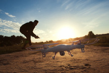 Close-up Of Flying Drone At Sunset, Free Space On Sky Background. Silhouette Of Young Man, Piloting Quadrocopter Outdoor. Leisure, Entertainment, Innovation, Modern Technologies Concept