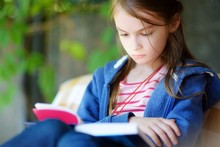 Cute Little Girl Reading A Book Outdoors