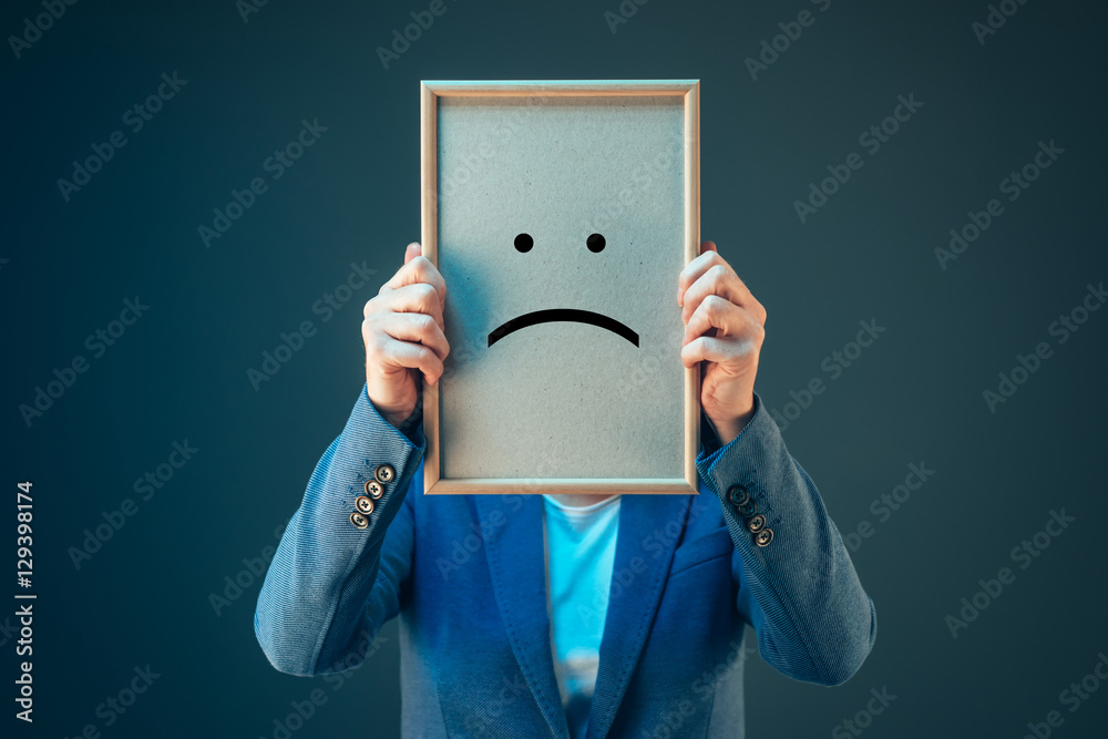 Businesswoman is pessimistic, holding smiley emoticon over face - obrazy, fototapety, plakaty 