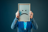Fototapeta  - Businesswoman is pessimistic, holding smiley emoticon over face