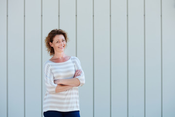 Wall Mural - Cheerful woman standing by wall with arms crossed