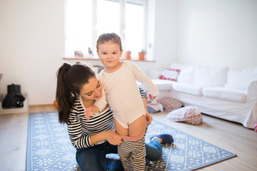 Wall Mural - Mother dressing her daughter in the morning their living room