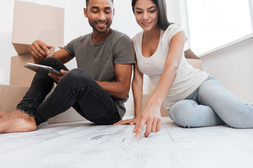 Wall Mural - Cheerful couple planning decoration at new home sitting on floor