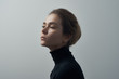 Leinwandbild Motiv Dramatic portrait of a young beautiful girl with freckles in a black turtleneck on white background in studio