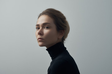 dramatic portrait of a young beautiful girl with freckles in a black turtleneck on white background 