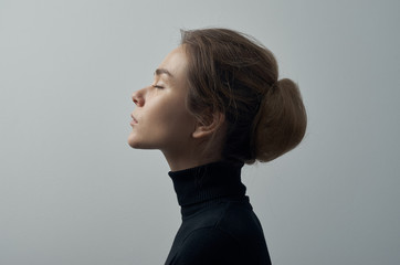 dramatic portrait of a young beautiful girl with freckles in a black turtleneck on white background 