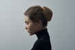 Dramatic portrait of a young beautiful girl with freckles in a black turtleneck on white background in studio
