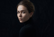 Dramatic portrait of a young beautiful girl with freckles in a black turtleneck on black background in studio