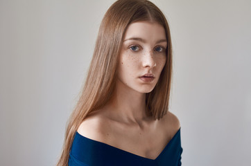 Beauty theme: portrait of a beautiful young girl with freckles on her face and wearing a blue dress on a white background in studio