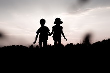 Silhouettes Of Kids Jumping Off A Cliff At Sunset. Little Boy And Girl Jump High Holding Hands. Brother And Sister Having Fun In Summer. Friendship, Freedom Concept. 
