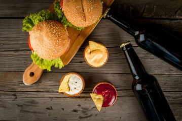 Selection of different food for a party: chips, nachos with sauces (tomato, cheese and mayonnaise tartar), burgers and beer, copy space 