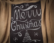 Merry Christmas hand drawn lettering with chalk on blackboard framed by golden curtains. Elegant unique design with snowflakes and Christmas tree