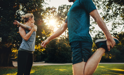 Wall Mural - Young couple warming up for morning workout in the park