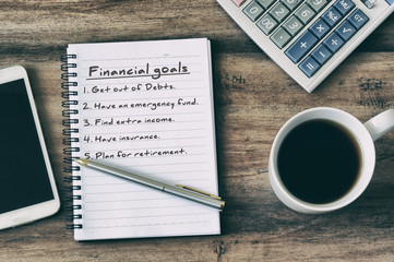 Wall Mural - Financial goals on notepad on blank notepad with calculator, coffee, pen and smart phone on a wooden table, retro style.