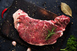 Raw beef steak with rosemary and garlic on cutting board on dark background