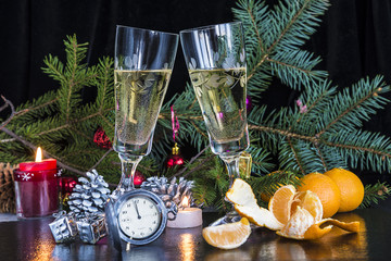 Christmas holidays with two glasses of champagne, burning candle and clock on black background