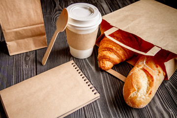 cup coffee and croissant in paper bag on wooden background