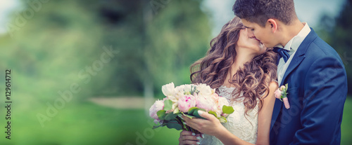 Fotomural Beautiful young bride and groom kissing in park