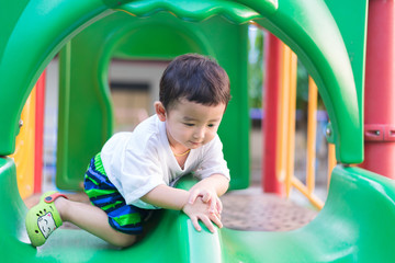 Wall Mural - Little Asian kid playing slide at the playground under the sunli