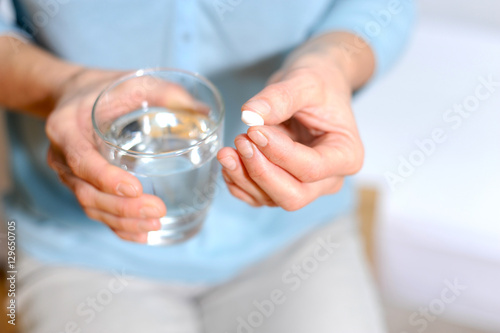 Fotografie, Obraz Frau hält eine Tablette und ein Glas Wasser in der Hand