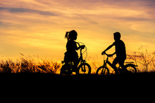   Silhouette Little Boy And Little Girl  Having Fun Riding Bike On Sunset  