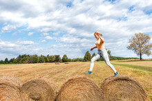 Young Woman Jumping Over Hay Roll Bales In A Field