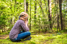 Young Woman Sitting On Mossy Ground In Forest Thinking