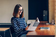 © gorynvd - Young beautiful smiling girl in stylish glasses and a warm sweater, reading the book in the co-working