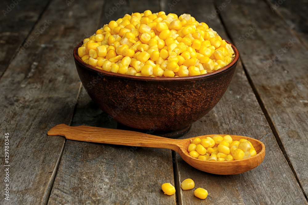 Bowl with corn seeds on wooden background