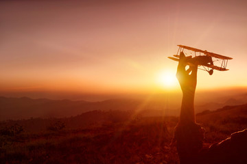 silhouette woman hand and toy airplane in the sunset.
