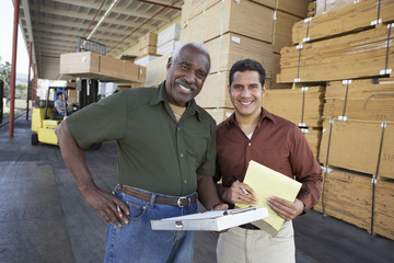 Portrait of two confident workers and man working with forklift in background