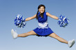 Full length of an excited young cheerleader jumping with pom-poms against sky