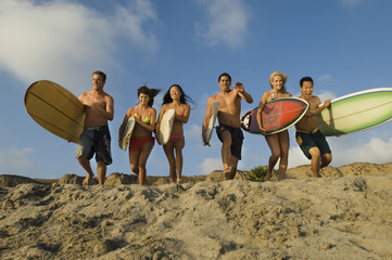 Group of multiethnic friends with surfboards running on sandy beach