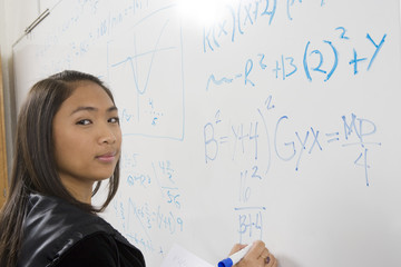 Portrait of an Asian female student solving mathematics problem on white board