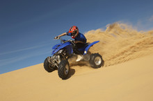 Low Angle View Of A Man Riding Quad Bike In Desert Against The Blue Sky