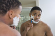 Young African American man shaving in front of bathroom mirror