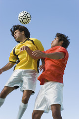 Low angle view of young soccer players heading ball against clear blue sky