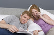 © moodboard - Happy young man reading novel while woman on call in bedroom