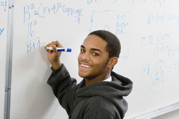 Portrait of smiling male student solving algebra equation on whiteboard in classroom