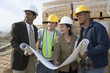 © MDBPIXS - Architects and workers with blueprint looking away at construction site