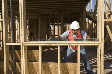 An African American man measuring level of a wooden beam with spirit level