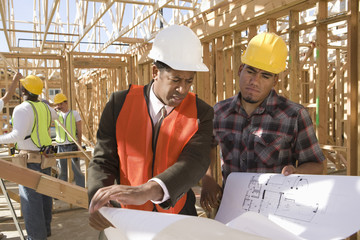 architect and foreman having discussion over blueprint with workers in background at construction si