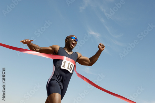 Fotomural Low angle view of an African American male runner winning race against blue sky