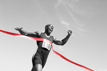 Low Angle View Of An African American Male Runner Crossing Finish Line Against Blue Sky